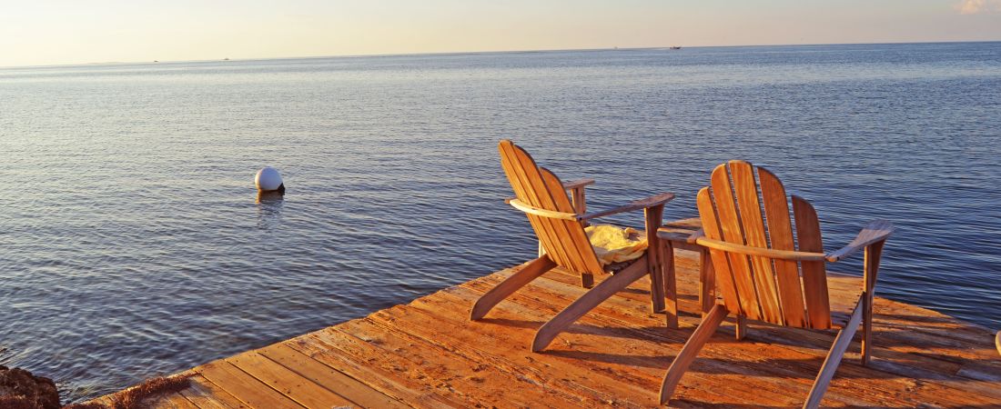 Wooden Adirondack chairs on the edge of a dock.