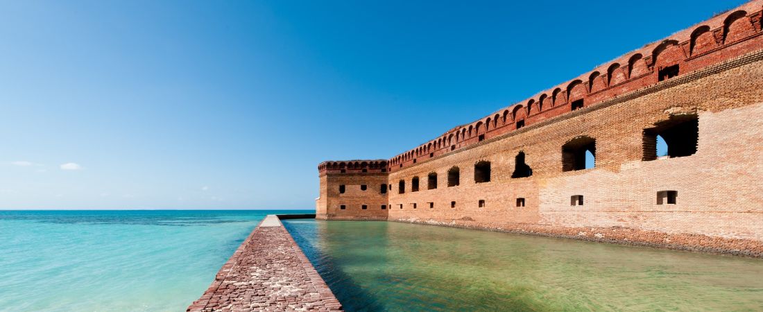 A Castle With A Clock Tower Next To A Body Of Water With Dry Tortugas National Park In The Background